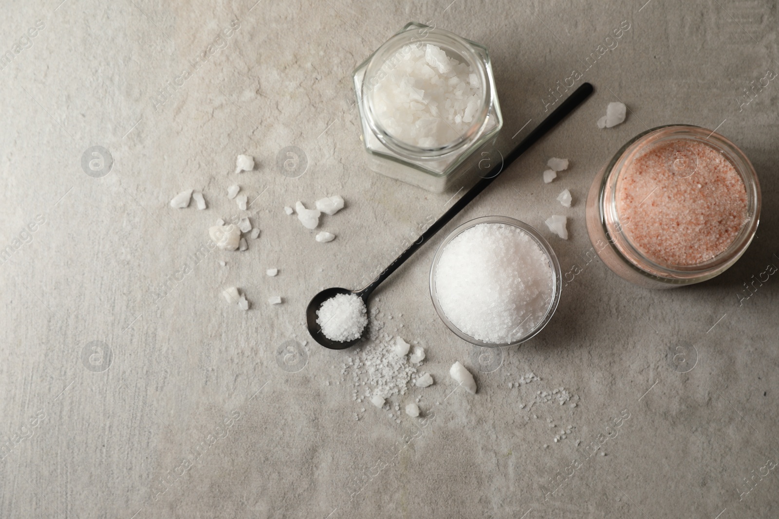 Photo of Different natural salt on grey textured table, flat lay. Space for text