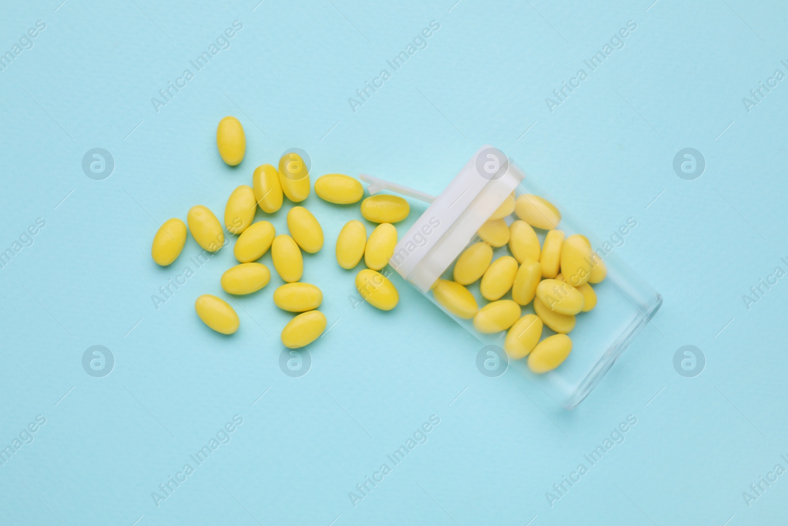 Photo of Tasty yellow dragee candies and container on light blue background, flat lay
