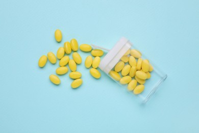 Photo of Tasty yellow dragee candies and container on light blue background, flat lay