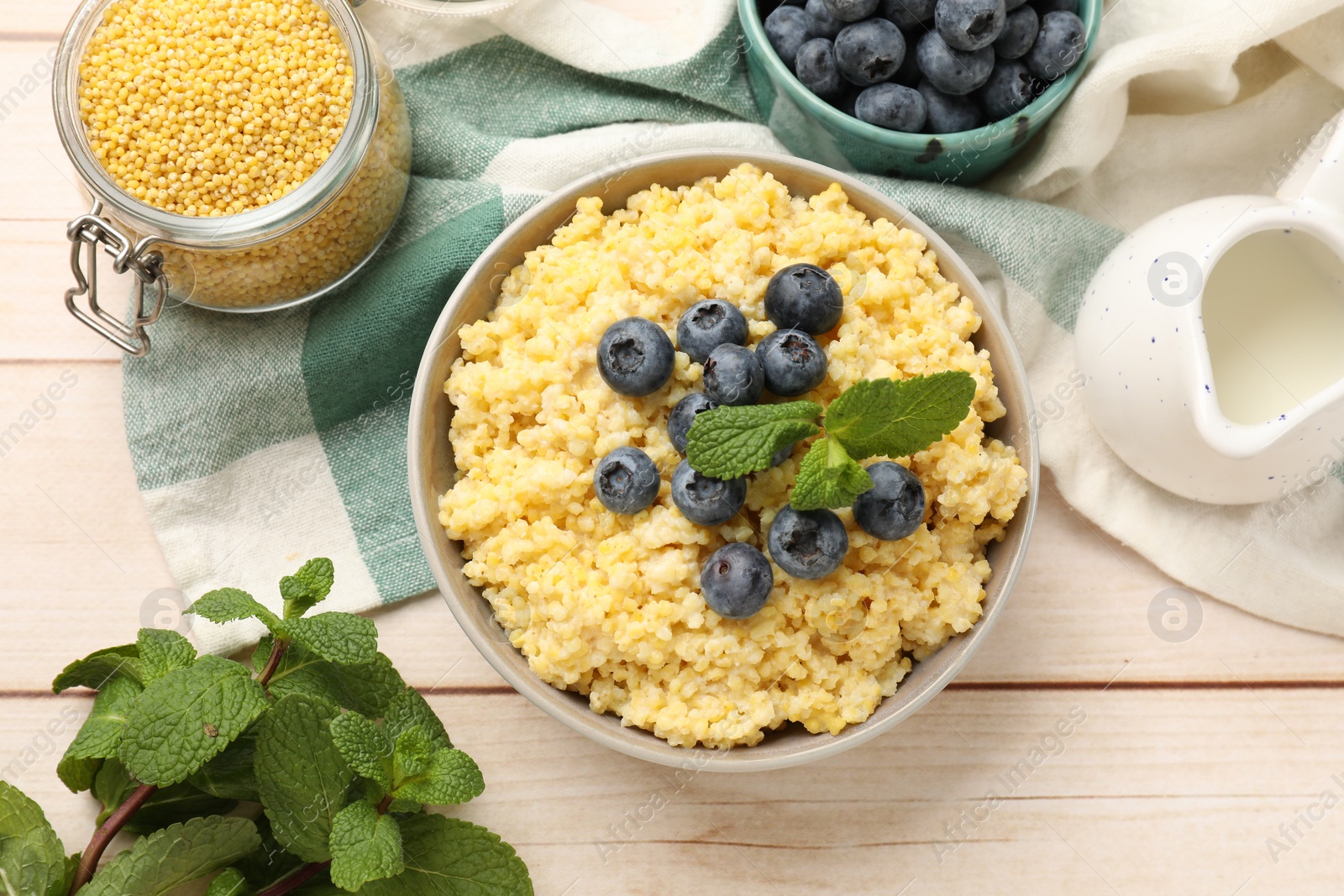 Photo of Tasty millet porridge with blueberries and mint in bowl on light wooden table, flat lay