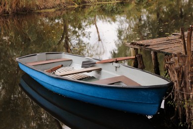 Photo of Light blue wooden boat with oars on lake near pier