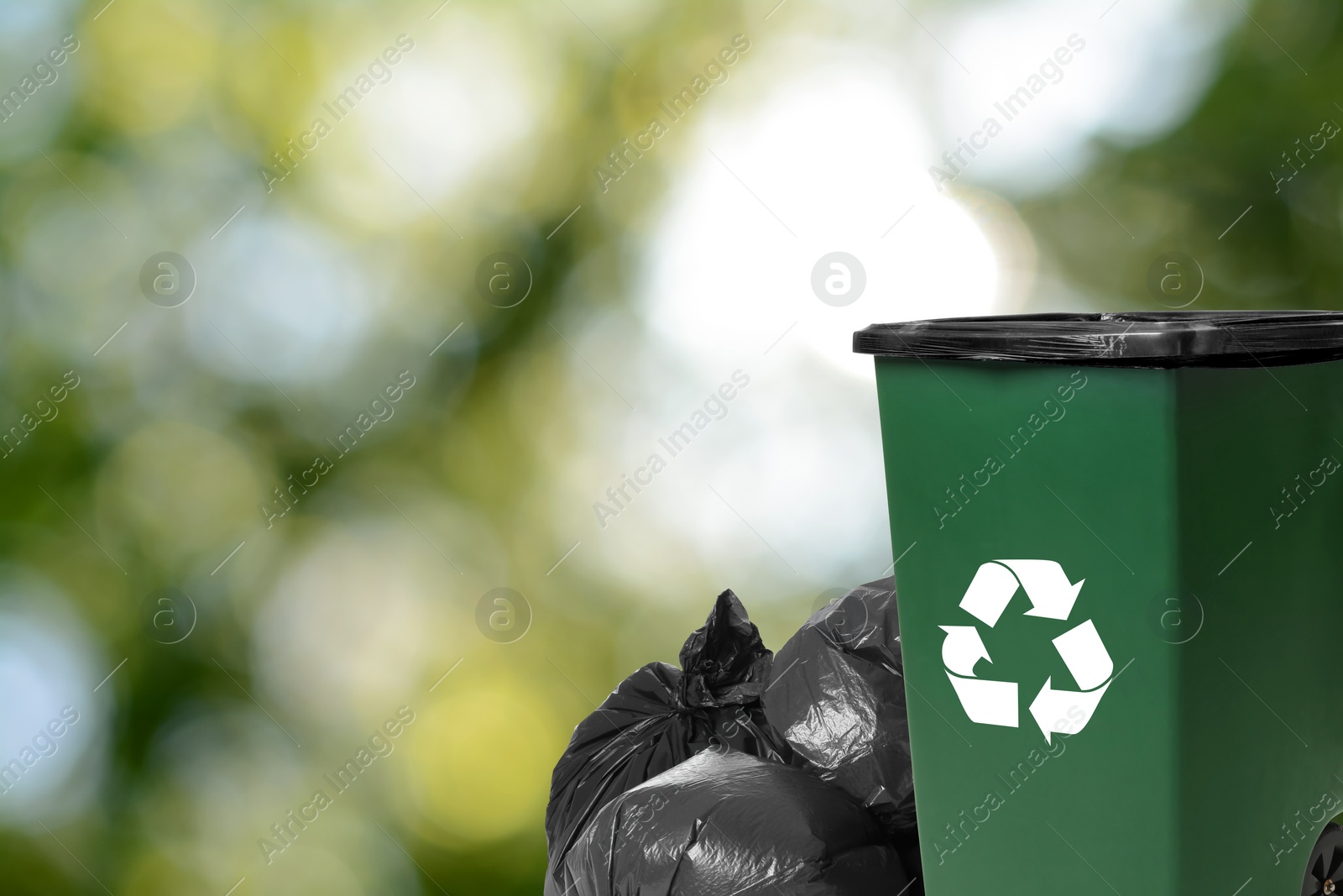 Image of Plastic bags full of garbage and waste bin on blurred background, space for text