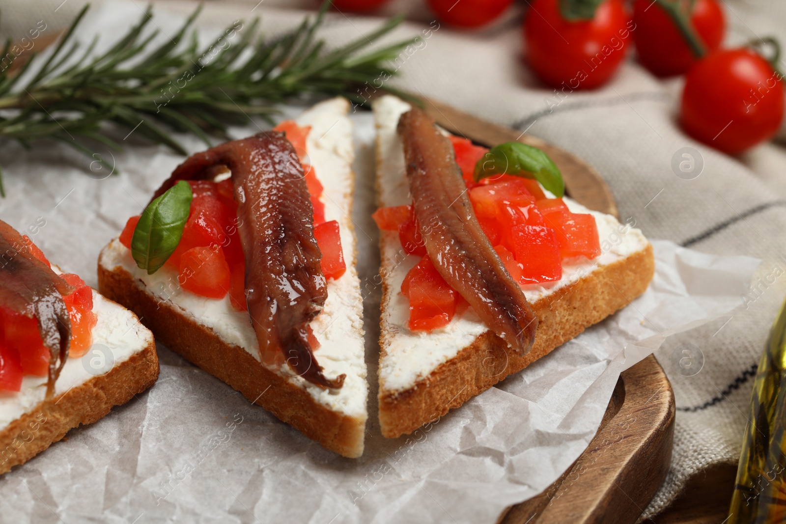 Photo of Delicious sandwiches with cream cheese, anchovies, tomatoes and basil on wooden board, closeup