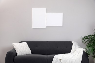 Photo of Blank canvas on wall over comfortable sofa indoors. Space for design