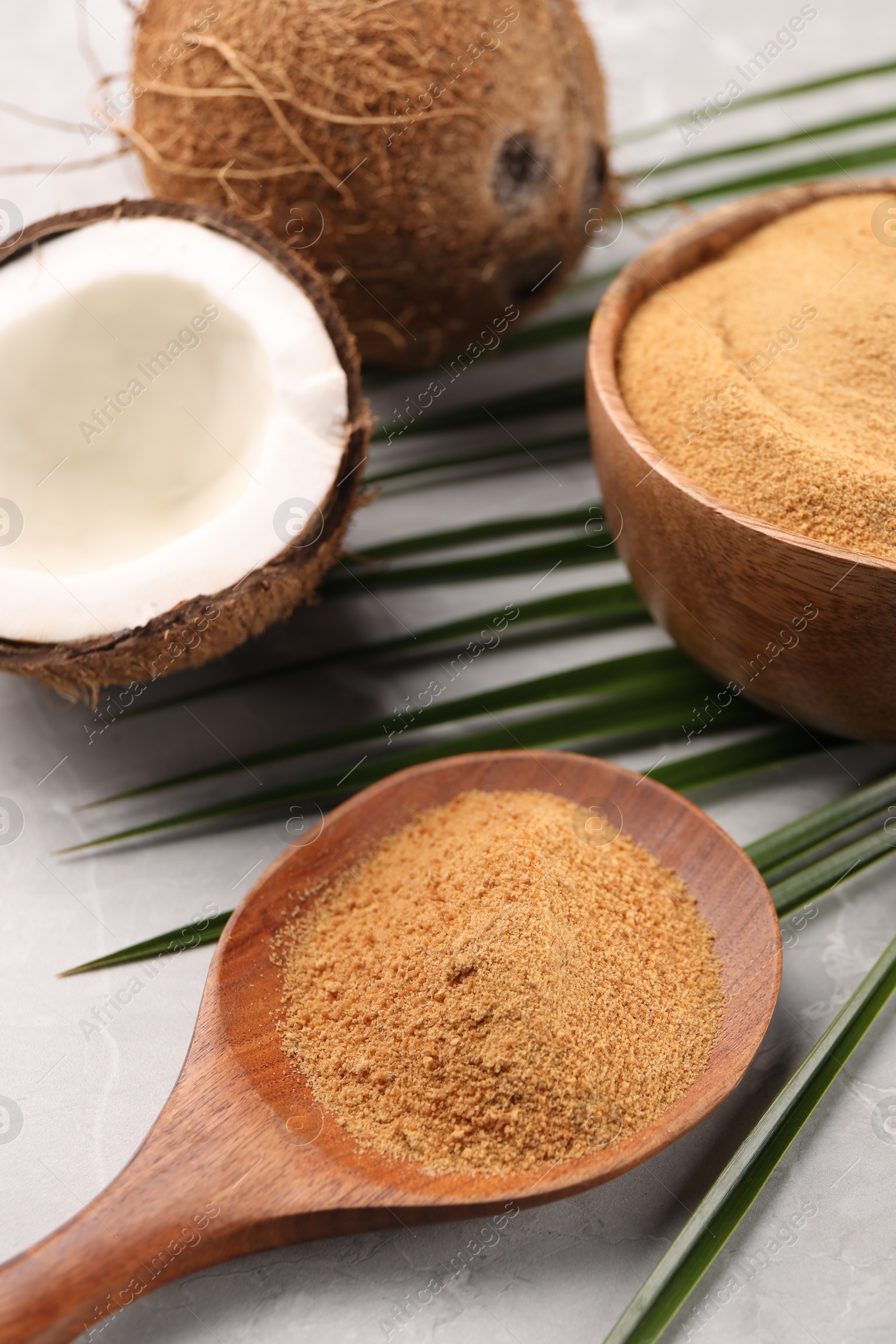 Photo of Spoon with coconut sugar, palm leaves, bowl and fruit on light marble table, closeup