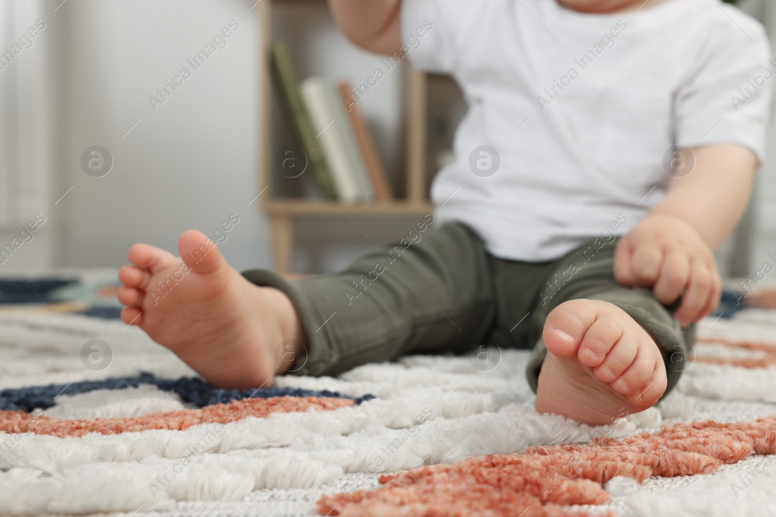 Photo of Baby sitting on soft carpet indoors, closeup