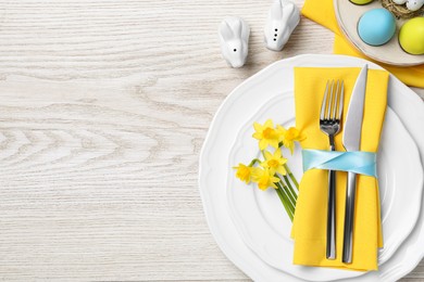 Photo of Festive table setting with painted eggs and cutlery on white wooden background, flat lay with space for text. Easter celebration