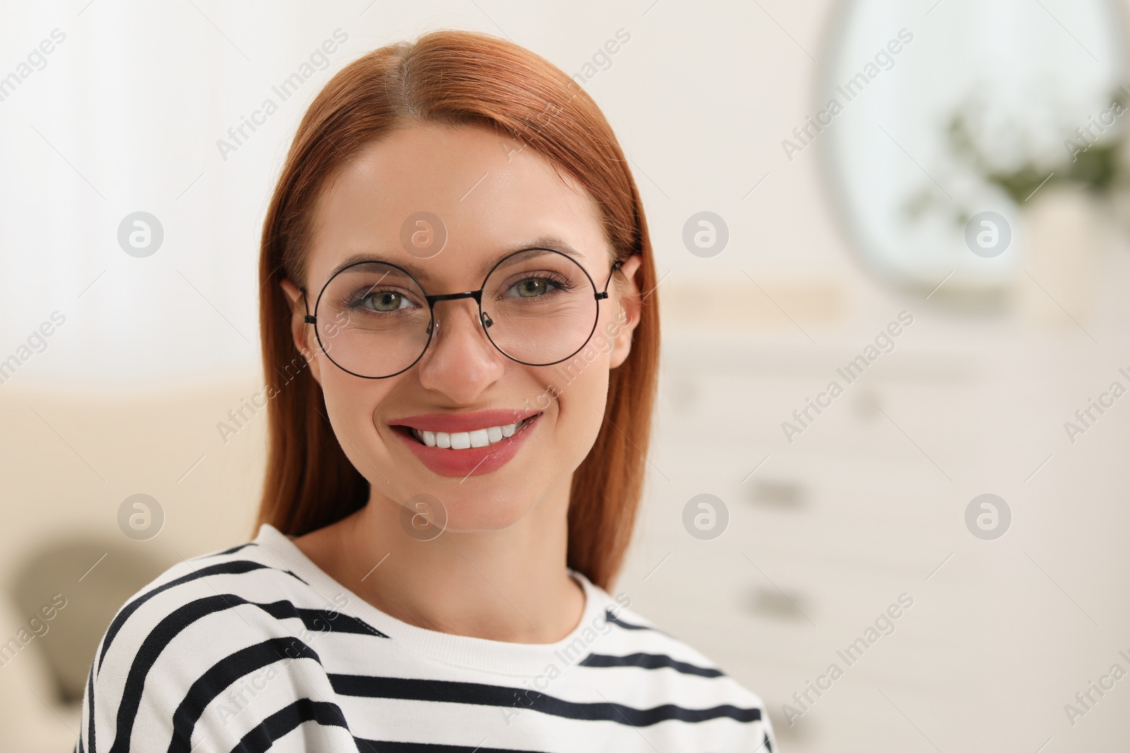 Photo of Portrait of beautiful young woman with red hair at home. Attractive lady smiling and looking into camera. Space for text