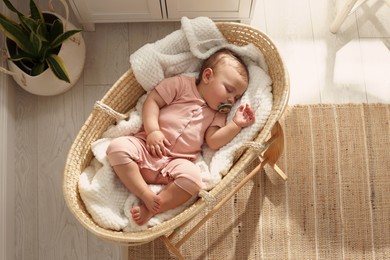 Photo of Cute little baby with pacifier sleeping in wicker crib at home, top view. Space for text