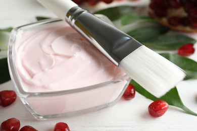 Photo of Glass bowl with natural facial mask, pomegranate seeds and brush on table, closeup