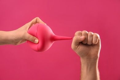 Photo of People demonstrating how to use enema on pink background, closeup