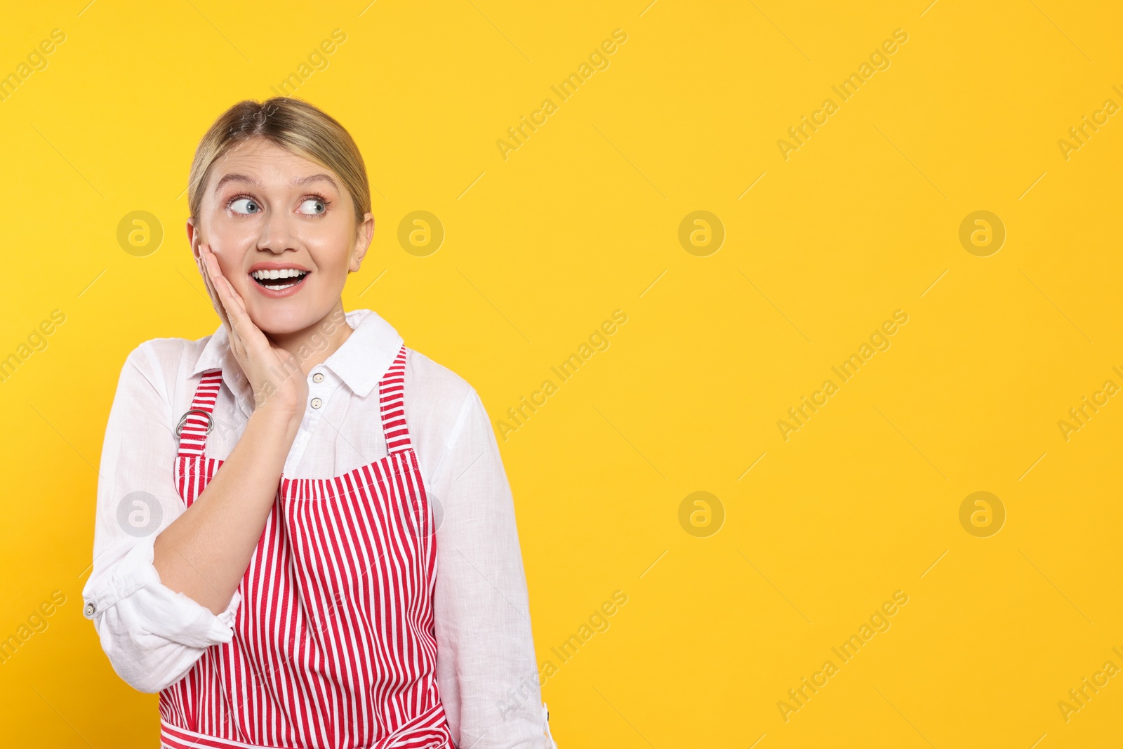 Photo of Beautiful young woman in clean striped apron on orange background. Space for text