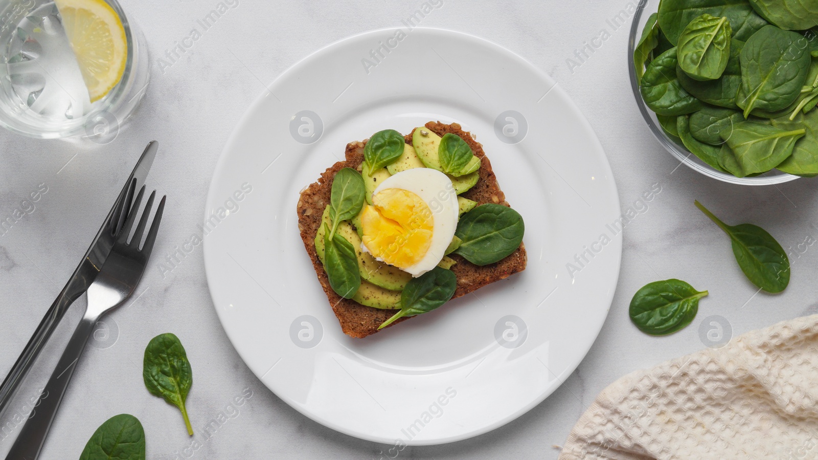 Photo of Tasty sandwich with boiled egg, avocado and spinach served on white marble table, flat lay