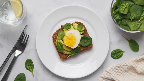 Tasty sandwich with boiled egg, avocado and spinach served on white marble table, flat lay