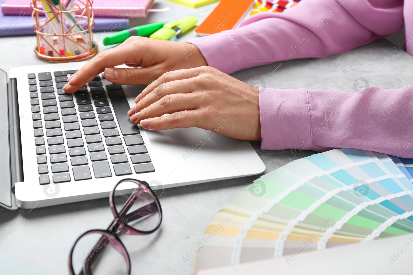 Photo of Woman working with laptop and palette samples at grey marble table, closeup