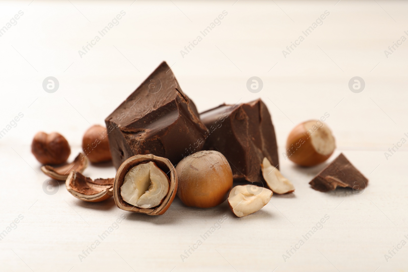 Photo of Delicious chocolate chunks and hazelnuts on white table