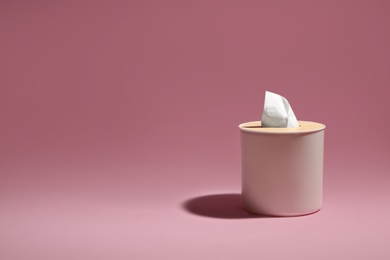 Photo of Holder with paper tissues on pink background. Space for text