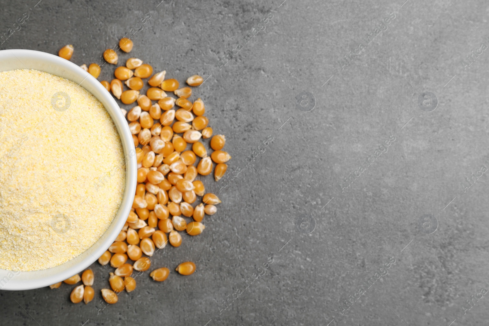 Photo of Bowl with corn flour and kernels on grey background, top view. Space for text