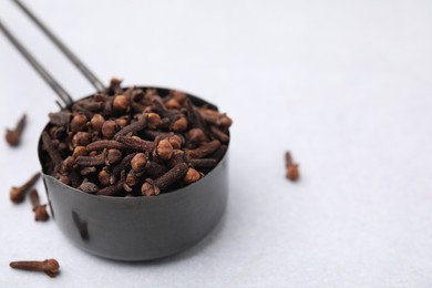 Photo of Aromatic cloves in scoop on light table, closeup. Space for text