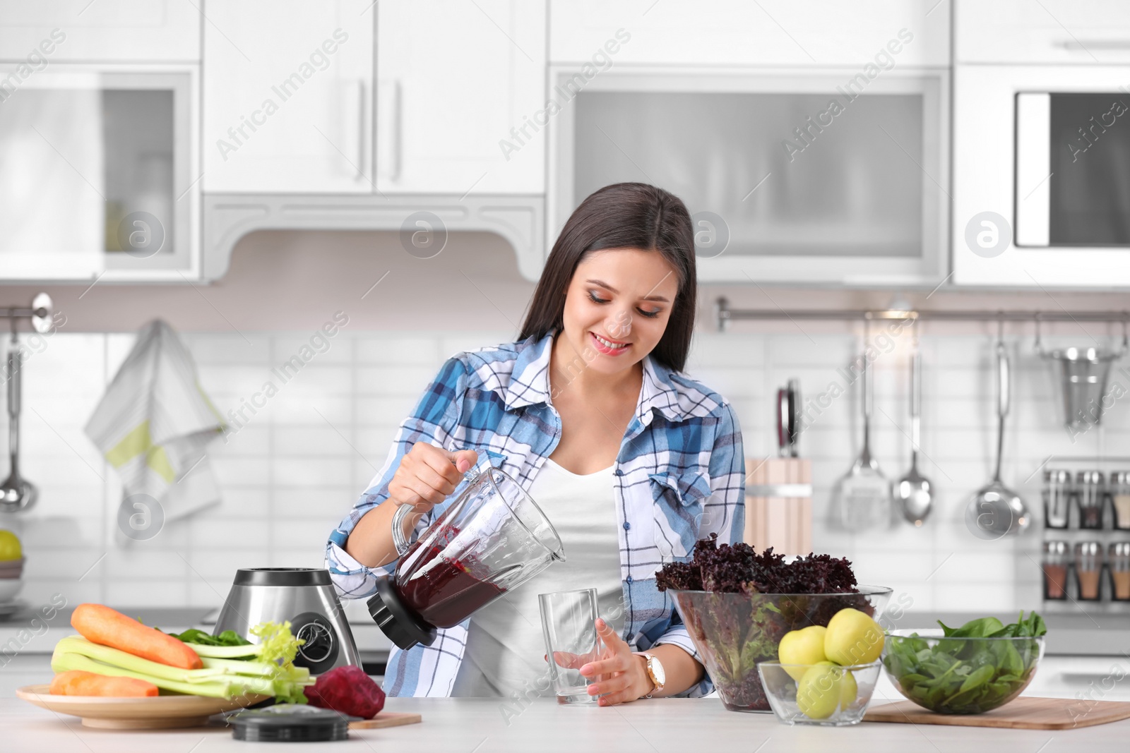 Photo of Young woman pouring tasty healthy smoothie into glass at table in kitchen