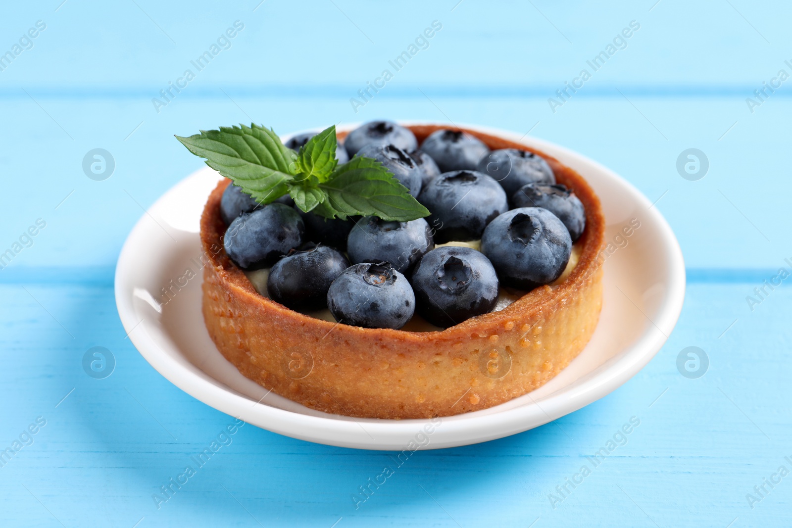 Photo of Tartlet with fresh blueberries on light blue wooden table, closeup. Delicious dessert