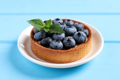 Photo of Tartlet with fresh blueberries on light blue wooden table, closeup. Delicious dessert