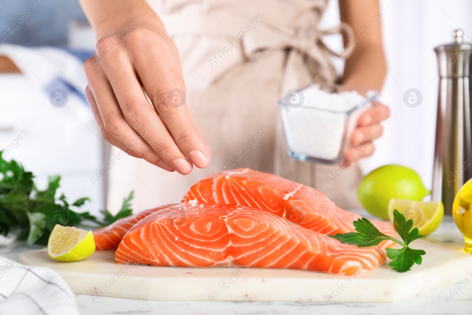 Photo of Woman salting fresh raw salmon at table, closeup. Fish delicacy