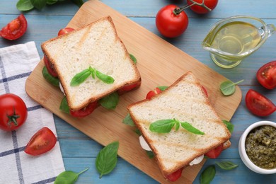 Photo of Delicious Caprese sandwiches with mozzarella, tomatoes, basil and pesto sauce on light blue wooden table, flat lay