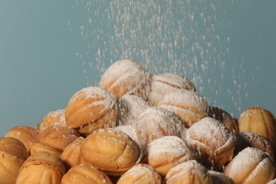 Photo of Sprinkling powdered sugar onto freshly baked walnut shaped cookies against light blue background, closeup. Homemade pastry filled with caramelized condensed milk