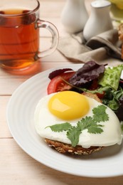 Plate with tasty fried egg, slice of bread and salad on light wooden table, closeup