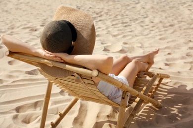 Young woman relaxing in deck chair on sandy beach