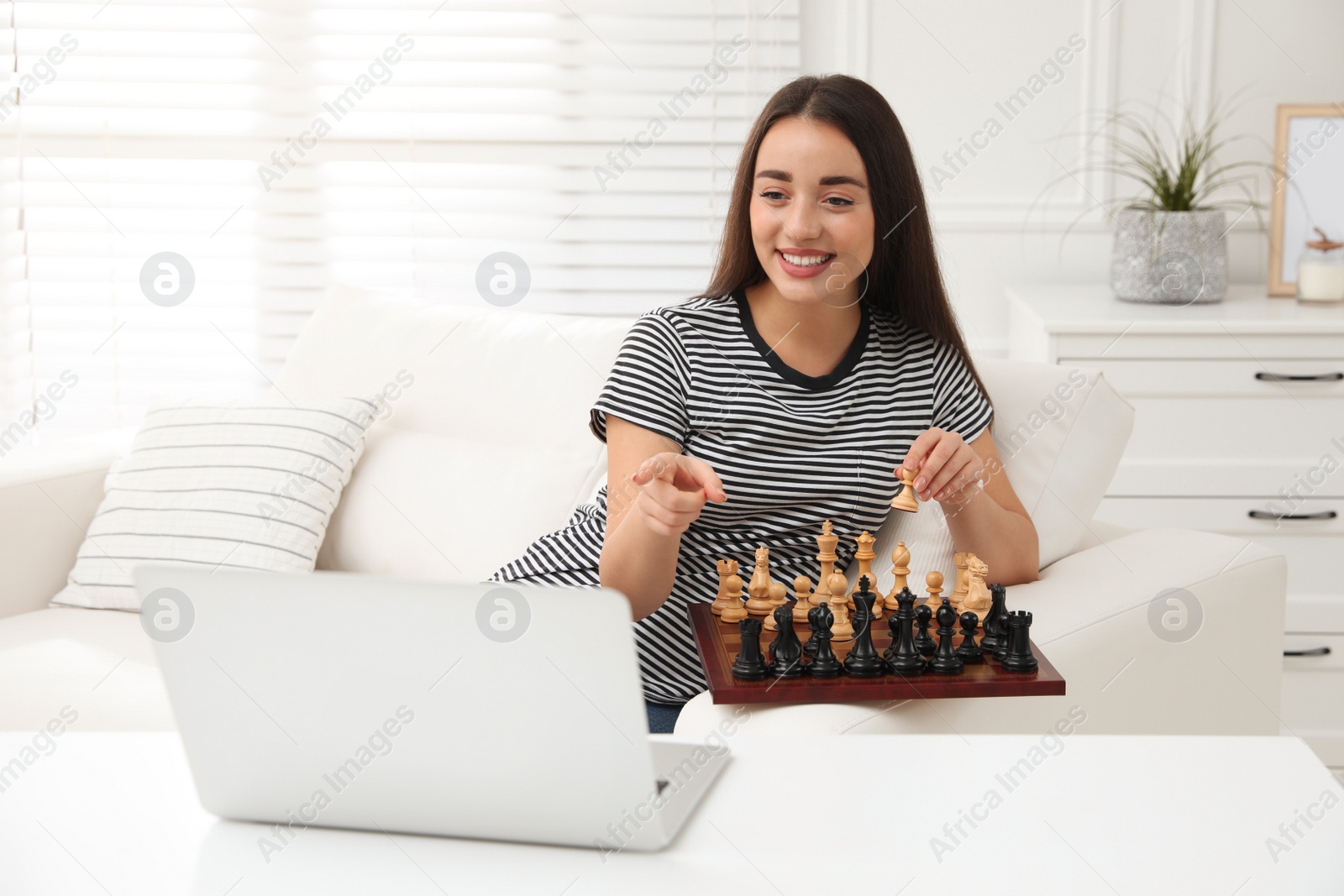 Photo of Young woman playing chess with partner through online video chat at home