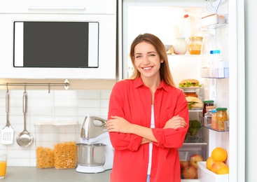 Happy young woman near open refrigerator in kitchen. Healthy diet