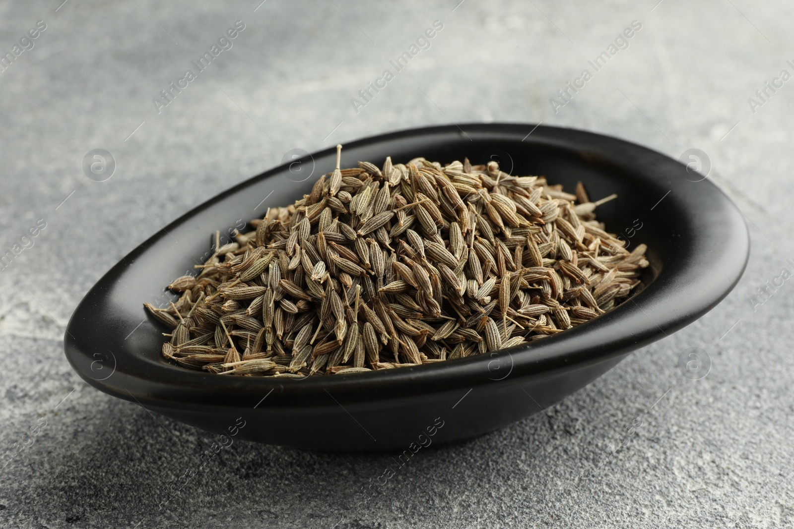 Photo of Caraway seeds in bowl on grey table, closeup