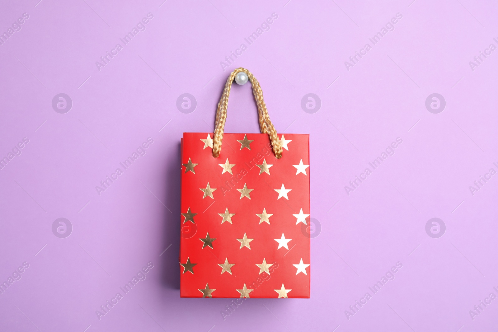 Photo of Red shopping paper bag with star pattern on violet background