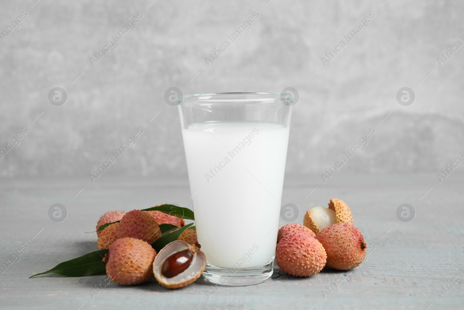 Photo of Fresh lychee juice and fruits on grey wooden table