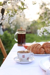 Stylish table setting with tea and croissants in spring garden