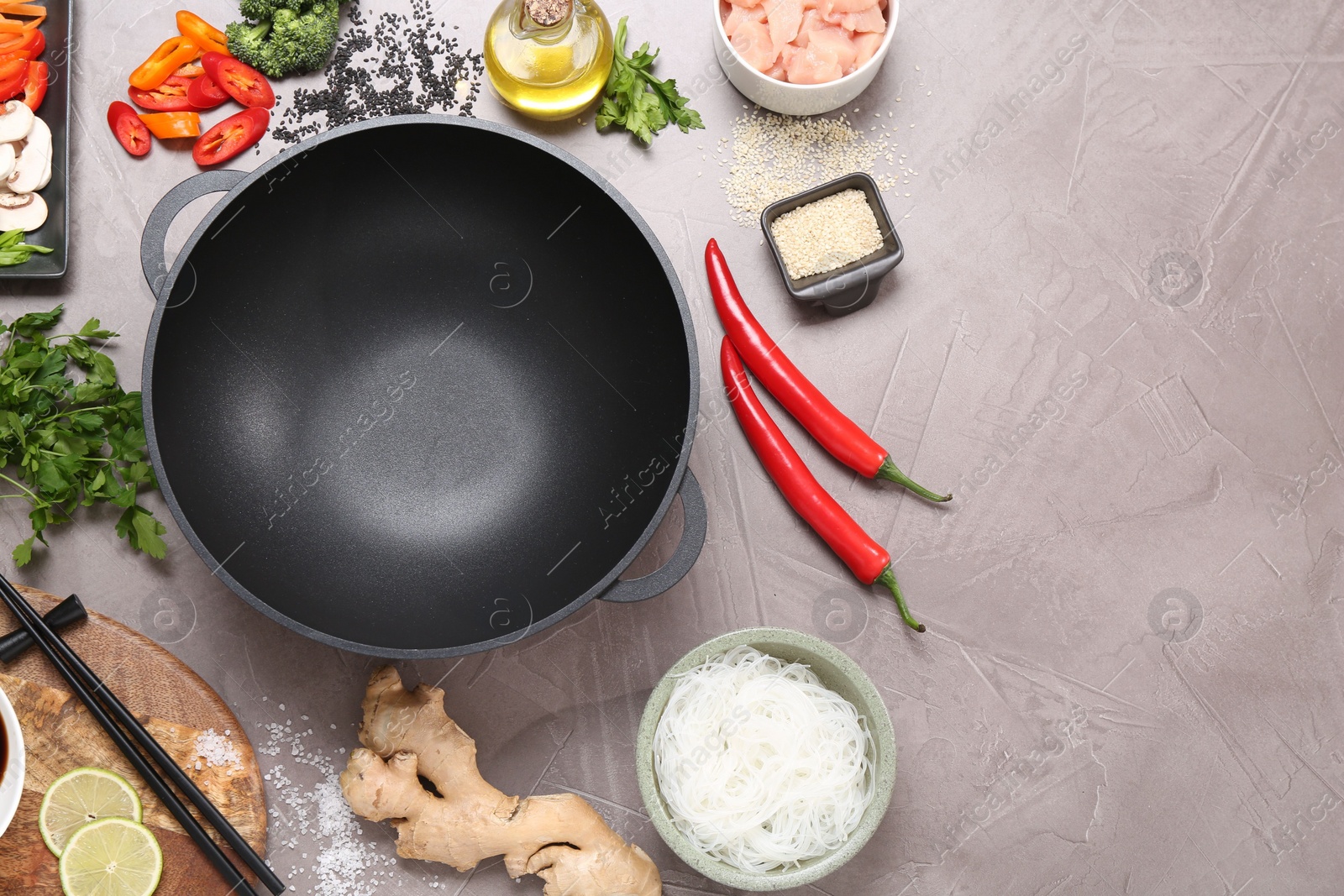 Photo of Wok, chopsticks and different products on grey textured table, flat lay. Space for text