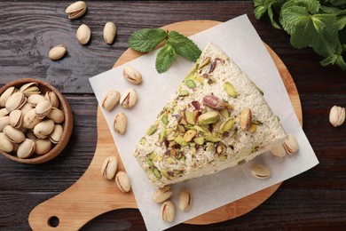 Photo of Piece of tasty halva with pistachios and mint on wooden table, flat lay