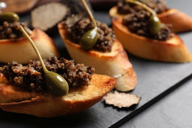 Tasty bruschettas with truffle paste and capers on black table, closeup