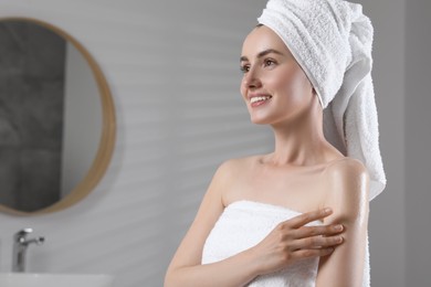 Photo of Happy woman applying body oil onto arm in bathroom, space for text