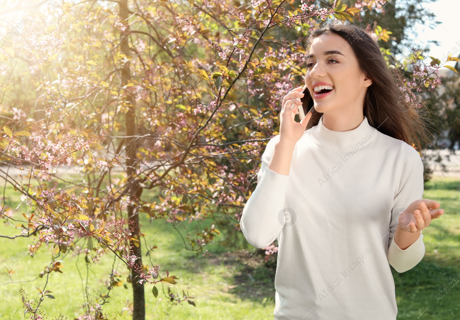 Photo of Young woman talking by phone outdoors on sunny day