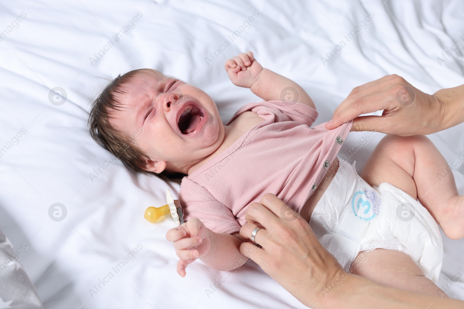 Photo of Mother putting clothes on crying daughter on bed, closeup