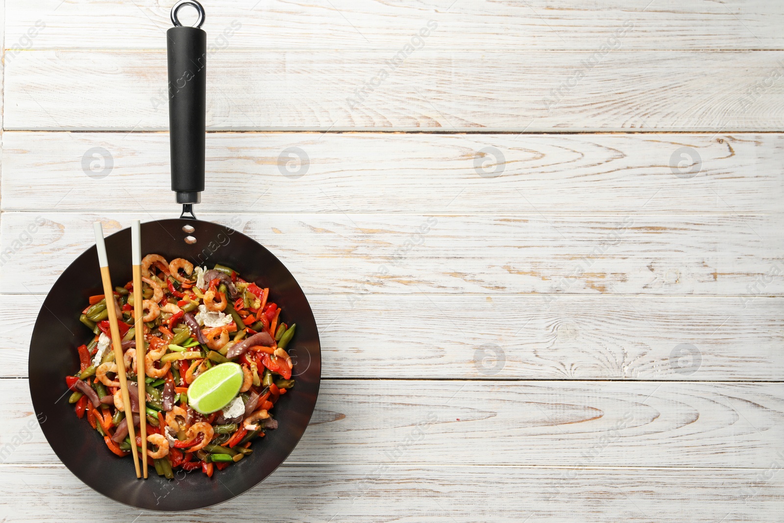 Photo of Shrimp stir fry with vegetables in wok and chopsticks on light wooden table, top view. Space for text