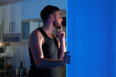 Man looking into refrigerator and choosing products in kitchen at night