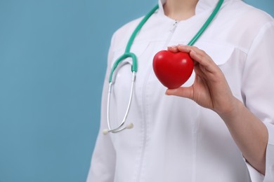 Doctor holding red heart on light blue background, closeup. Space for text