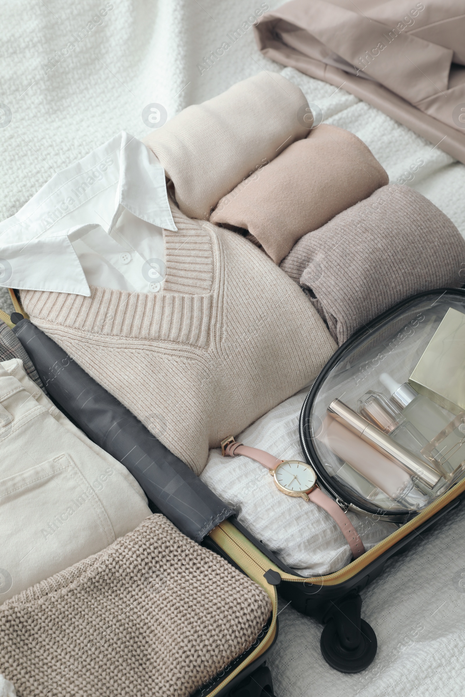 Photo of Open suitcase with folded clothes and accessories on bed