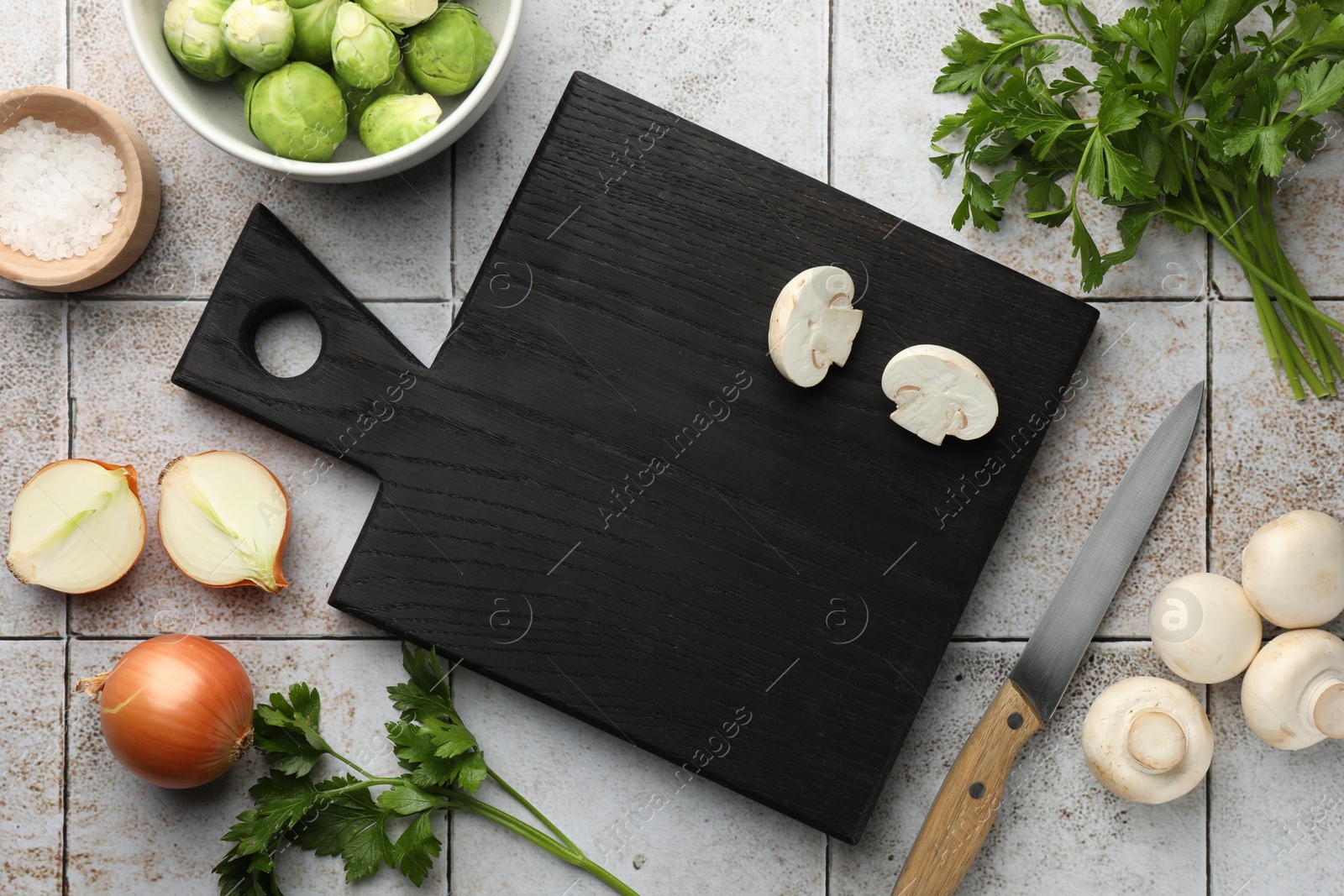 Photo of Flat lay composition with black cutting board and products on light tiled table