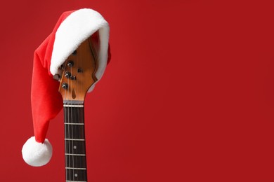 Photo of Guitar with Santa hat on red background, space for text