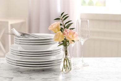 Photo of Set with clean dishes and vase of flowers on white marble table